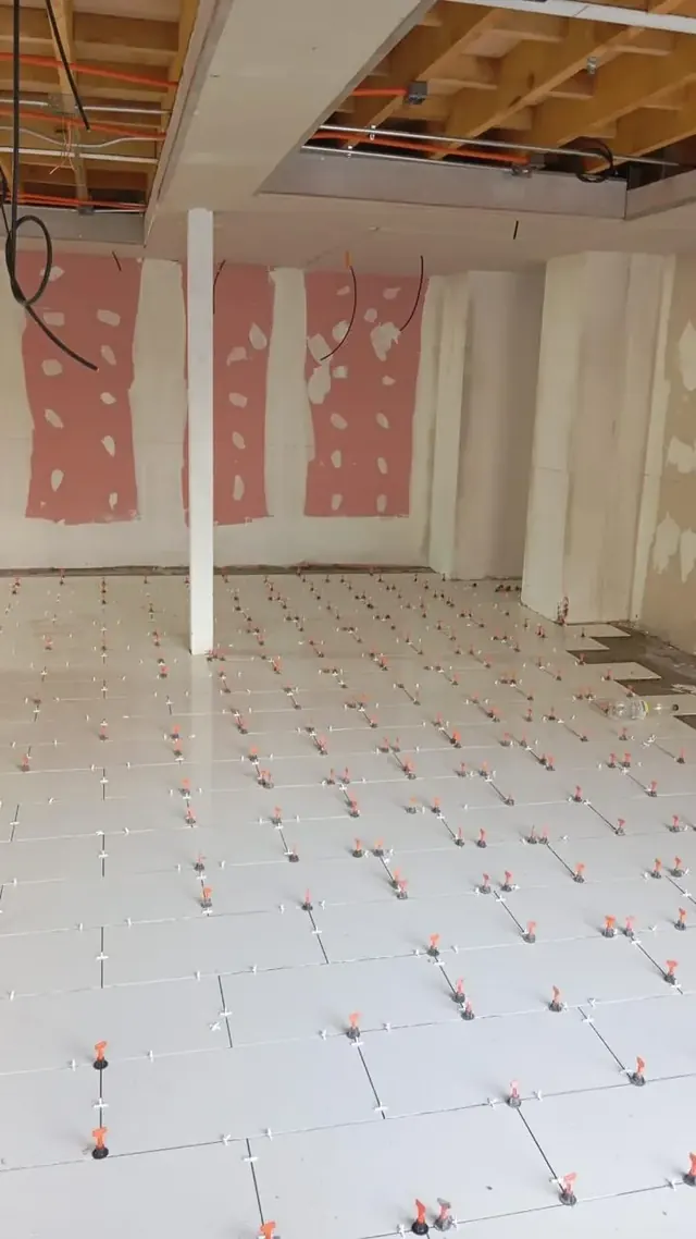 Vista del proceso de instalación de cerámica con niveladores en piso interior, asegurando precisión y uniformidad en los acabados. Cerámicas recién instaladas con sistema de nivelación en obra interior.