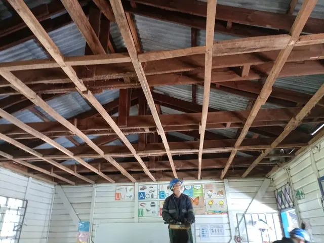 Proceso de retiro del cielo antiguo y refuerzo de estructura de techumbre en el aula de la Escuela Rural Bellavista. Trabajador reforzando estructura de techumbre durante el proceso de mejora en escuela rural.