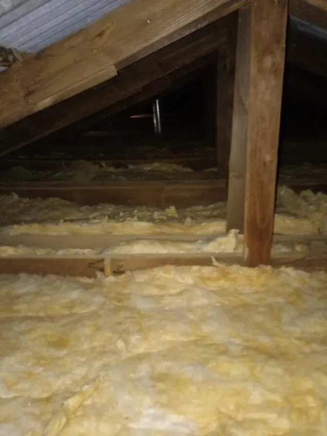 Detalle del entretecho con instalación de lana de vidrio para mejorar confort y eficiencia energética en escuela rural. Vista del entretecho con aislación de lana de vidrio instalada.