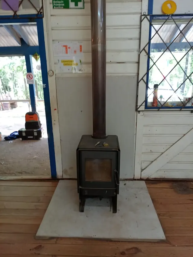 Resultado final del montaje de estufa a combustión lenta con base térmica y medidas de seguridad implementadas. Estufa instalada en aula con base de hormigón para seguridad y confort térmico.