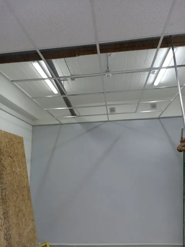 El cielo americano permite un acceso rápido a instalaciones técnicas manteniendo una estética profesional. Estructura de perfilería blanca para cielo americano con tubos LED de luz blanca instalados y algunas palmetas acústicas colocadas.