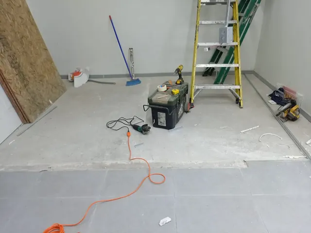 Primer plano de herramientas de construcción (lijadora, caja de herramientas, escalera) sobre un piso de concreto junto a un sector de porcelanato gris terminado. Primer plano de herramientas de construcción (lijadora, caja de herramientas, escalera) sobre un piso de concreto junto a un sector de porcelanato gris terminado.