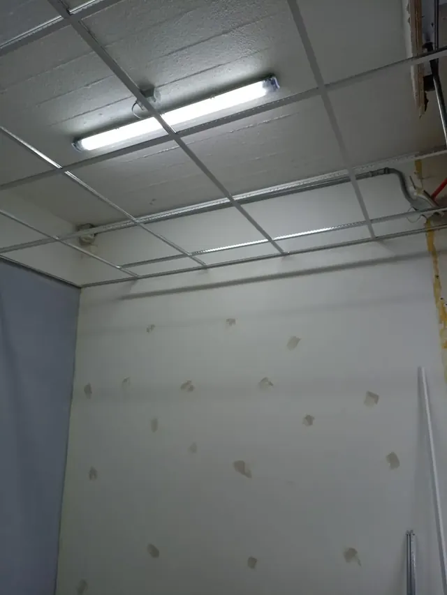 Nivelación y tratamiento de muros para asegurar un acabado de pintura impecable y de larga duración. Pared blanca con parches de pasta muro gris para tapar imperfecciones, bajo el sistema de cielo americano en proceso.