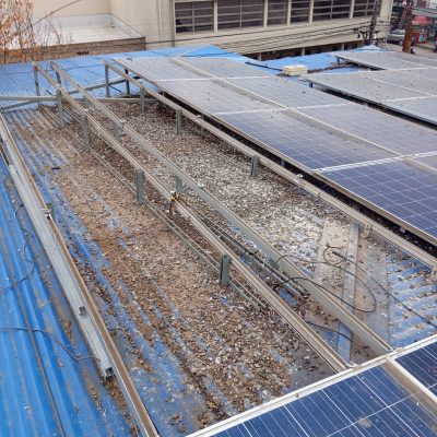 Vista superior de techumbre azul con paneles solares y residuos acumulados.
