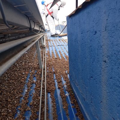 Personal con arnés realizando limpieza bajo paneles solares en cubierta azul.