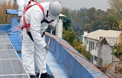 Trabajadores limpiando techumbre azul con arnés de seguridad.