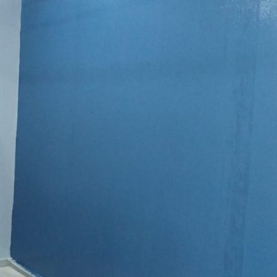 Muro con pintura fresca de color azul sólido bajo una estructura de cielo americano; se ven implementos de limpieza en el suelo de concreto.