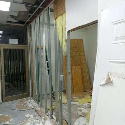 Fase de demolición mostrando la perfilería de acero galvanizado de un tabique, con paneles de aislación de lana de vidrio expuestos y escombros en el suelo.