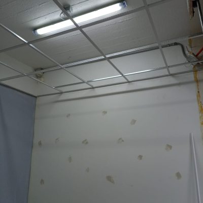 Pared blanca con parches de pasta muro gris para tapar imperfecciones, bajo el sistema de cielo americano en proceso.